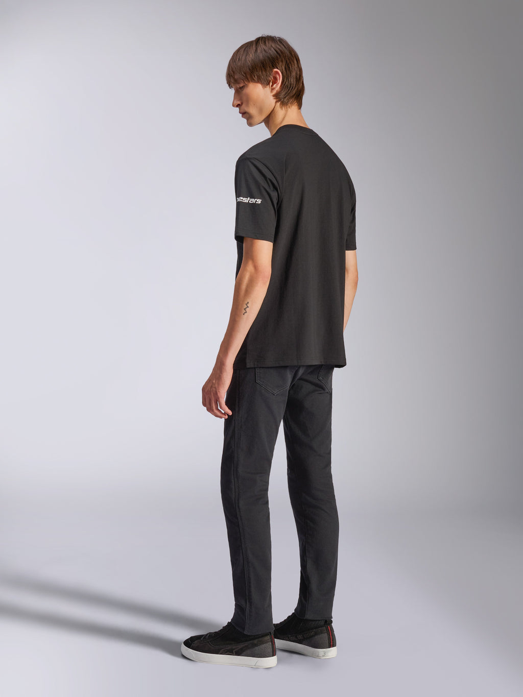 Alpinestars Frontal CSF Tee, T-shirt met korte mouwen, zwart, witte Astars-branding op de mouw, gedragen door model met zwarte broek en schoenen, casual motorsport-geïnspireerd ontwerp