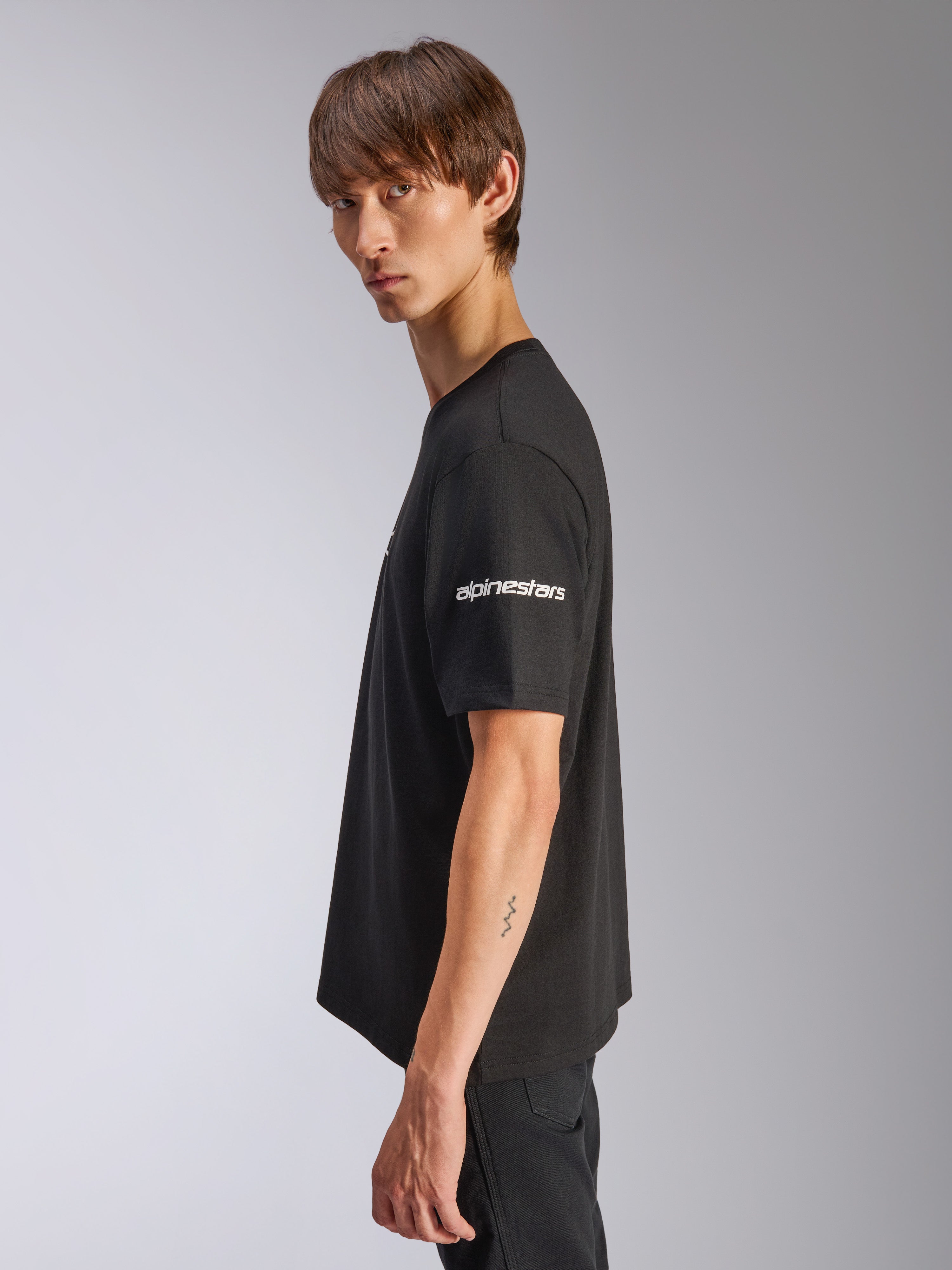 Alpinestars Frontal CSF Tee, T-shirt met korte mouwen, zwart, wit Alpinestars-logo op de mouw, gedragen door model in profielaanzicht, casual motorsport performance streetwear