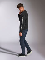 Alpinestars Trackside CSF T-shirt met lange mouwen, zwart met wit verticaal Alpinestars-woordmerk op de mouw, gedragen door een model met donkere denim en sneakers, casual motorsport-geïnspireerde sportkleding