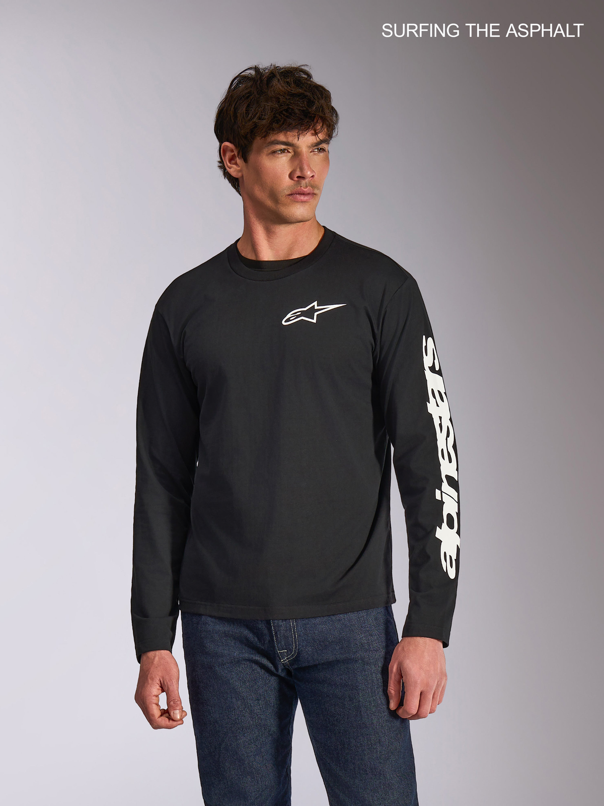 T-Shirt Trackside CSF d'Alpinestars, t-shirt casual à manches longues pour homme en noir, avec le logo Ride 4.0 blanc à l'avant et la marque imprimée sur la manche, porté par un mannequin avec un jean
