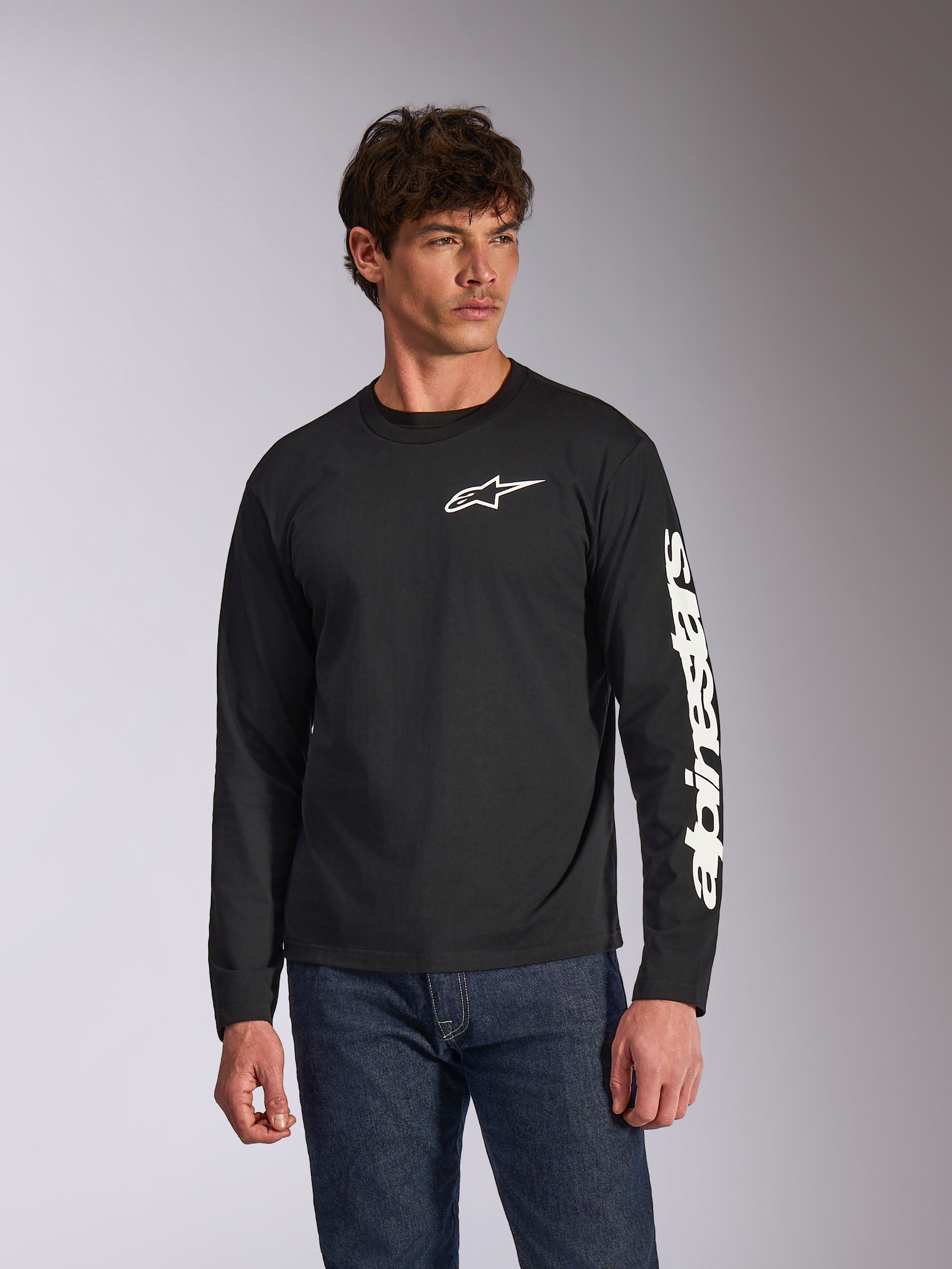Alpinestars Trackside CSF Long Sleeve Tee, zwart shirt met lange mouwen, wit Alpinestars-logo op de borst en merknaam op de mouw, gedragen door een model met blauwe jeans, casual motorsport streetwear