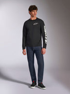 Alpinestars Trackside CSF Tee, T-shirt met lange mouwen, zwart en wit, gedragen met donkerblauwe jeans en zwarte sneakers, voorzien van wit Ride 4.0 logo op de borst en Alpinestars woordmerk op de mouw, casual motorsport-geïnspireerde streetwear