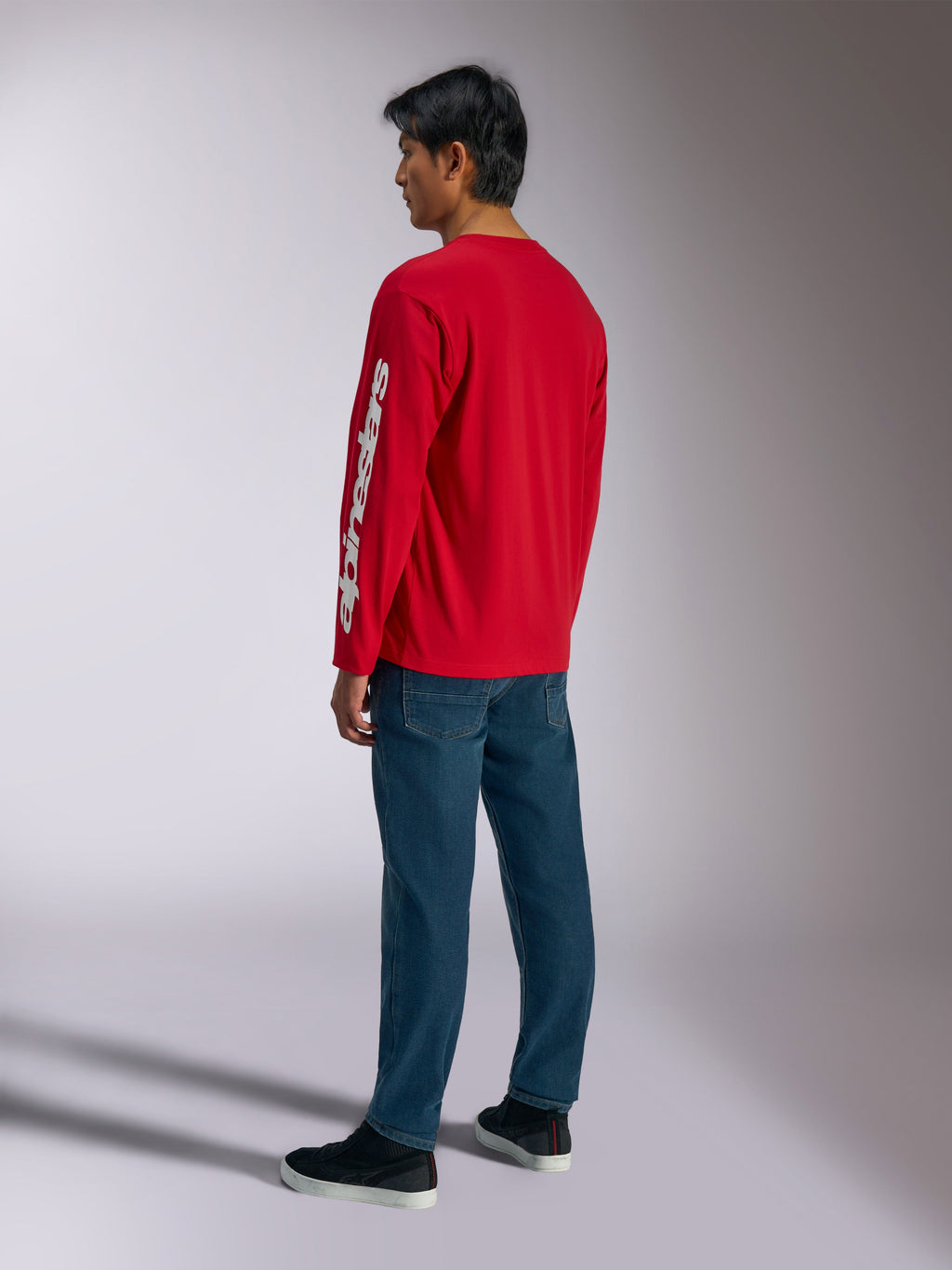 Alpinestars Trackside CSF Tee, T-shirt met lange mouwen, rood, met een wit verticaal Alpinestars-logo op de mouw, gedragen door een model met blauwe jeans en zwarte sneakers, casual op motorsport geïnspireerde streetwear