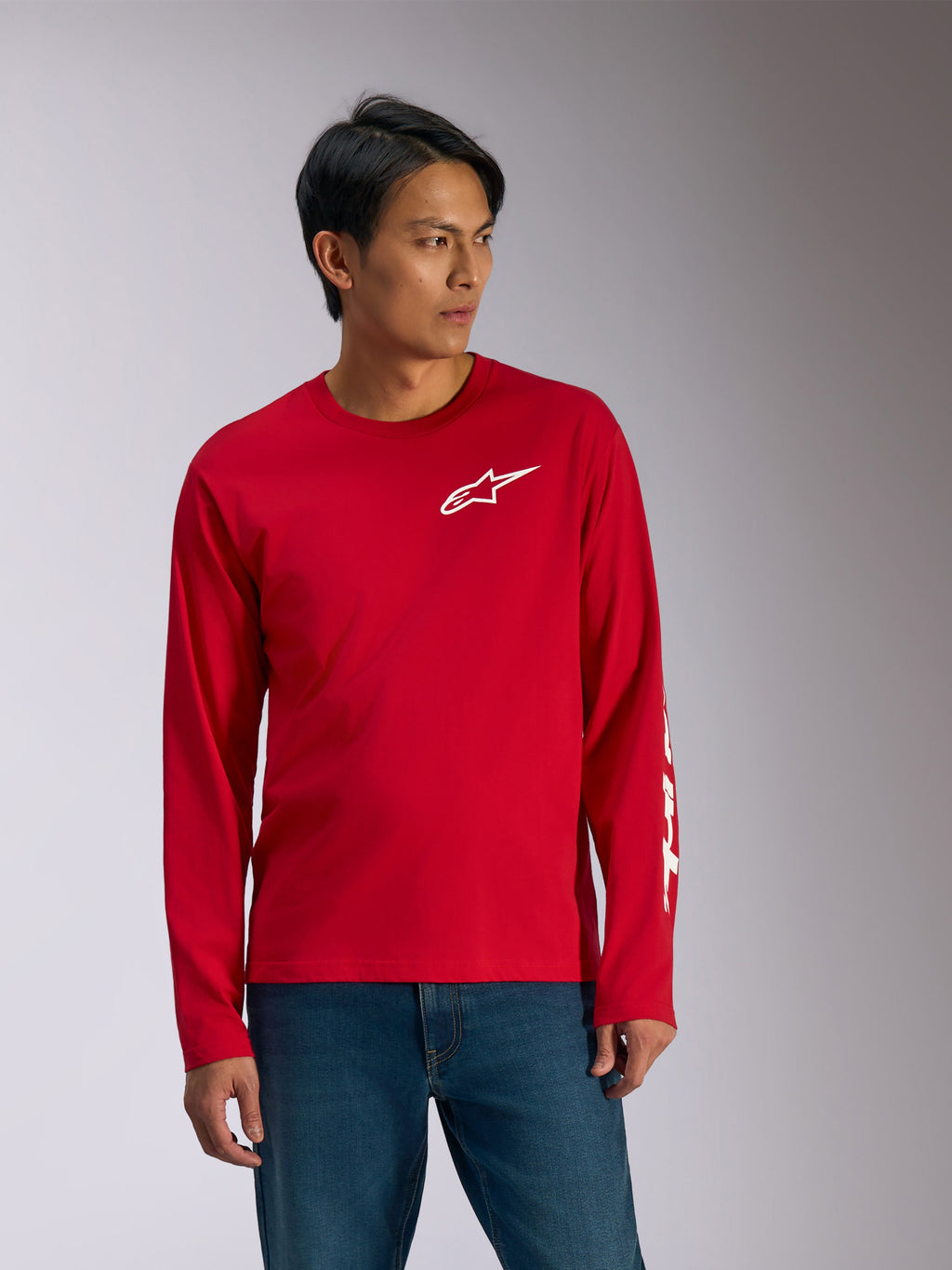 Alpinestars Trackside CSF Tee, T-shirt met lange mouwen, rood met witte graphics, wit Alpinestars sterlogo op de borst en witte tekst op de mouw, gedragen met blauwe jeans, casual motorsport-geïnspireerde sportkleding