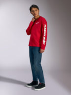 Alpinestars Trackside CSF Long Sleeve Tee, rood met witte Alpinestars-branding op de borst en mouw, gedragen door model met blauwe jeans en zwarte sneakers, casual motorsport-geïnspireerde streetwear