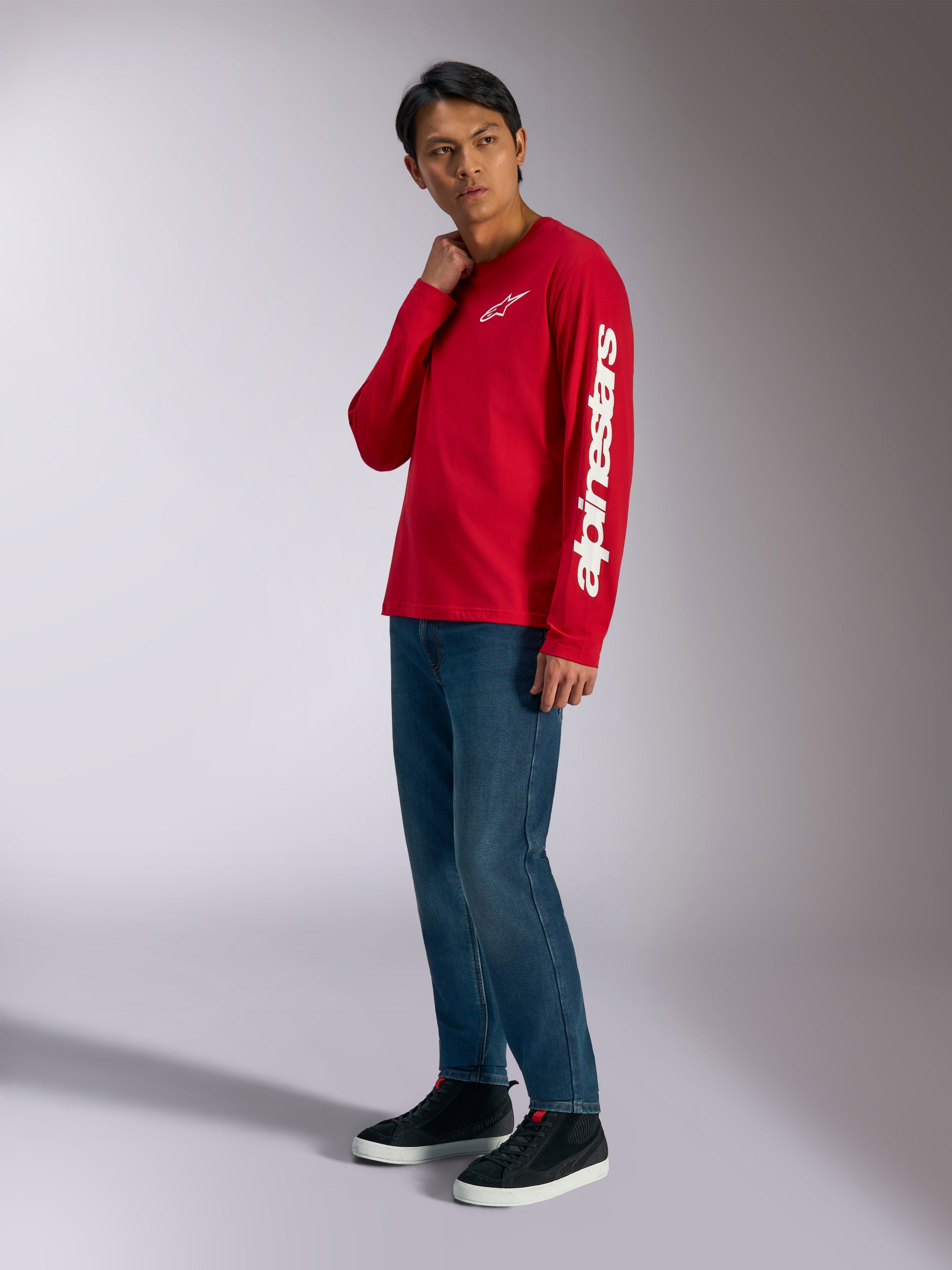 Alpinestars Trackside CSF Long Sleeve Tee, rood met witte Alpinestars-branding op de borst en mouw, gedragen door model met blauwe jeans en zwarte sneakers, casual motorsport-geïnspireerde streetwear