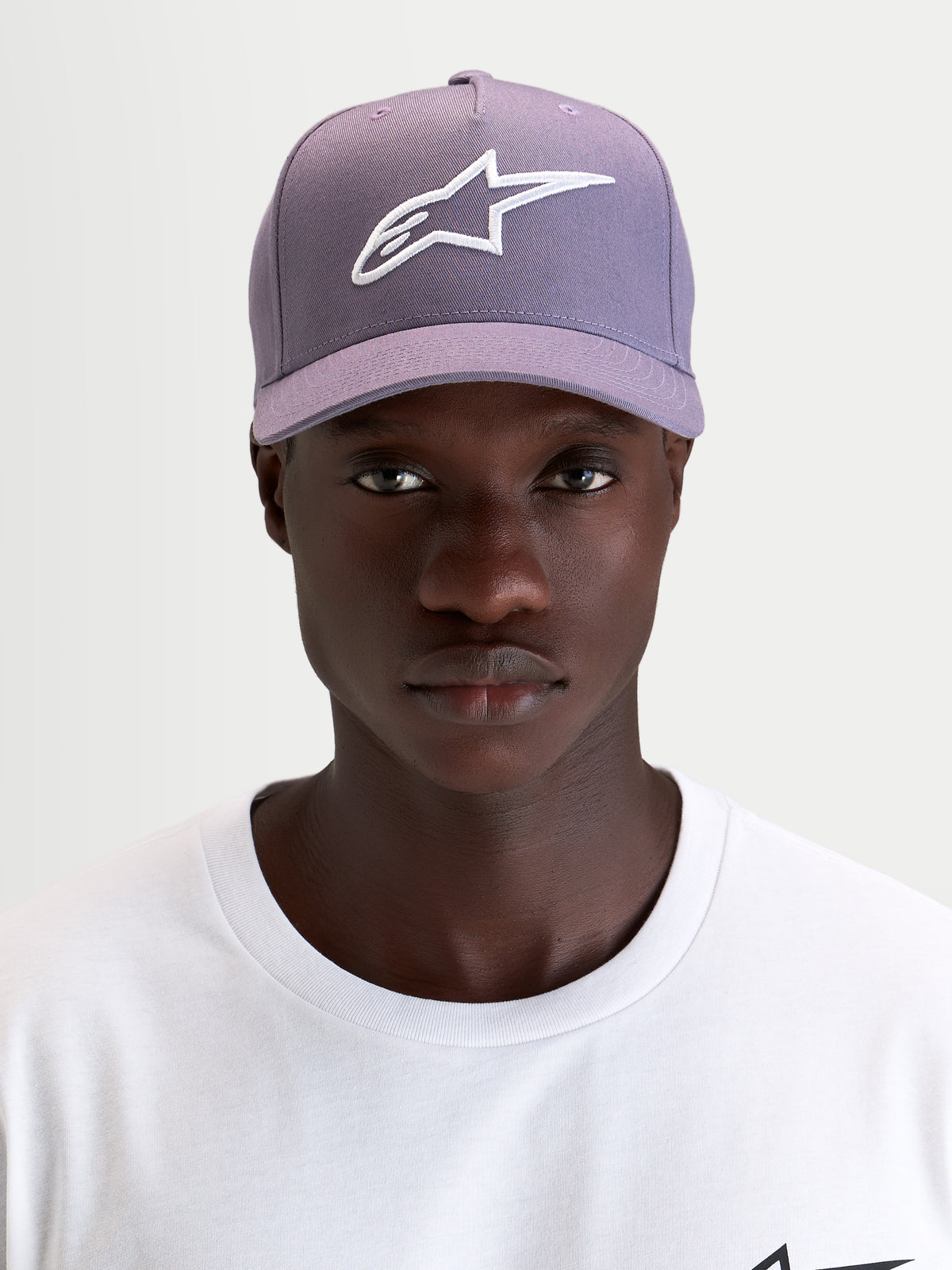 Alpinestars Casquette Snapback Ageless, casquette sportswear violette et blanche, portée par un modèle mettant en valeur le logo Astars brodé 3D sur l'avant et le profil structuré
