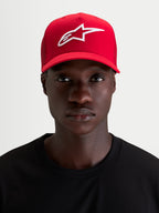 Alpinestars Ageless Snapback Kappe, rote Sportswear-Kappe getragen von einem Model, mit weißer 3D-Stickerei des Astars-Logos, gebogenem Schirm und strukturierter Baumwoll-Twill-Konstruktion