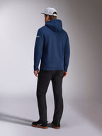 Alpinestars Frontal Hoodie, achteraanzicht van een marineblauwe pullover fleece hoodie, wit woordlogo op de mouw, gecombineerd met een zwarte broek en een witte mesh truckerpet, casual op motorsport geïnspireerde streetwear