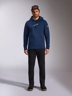 Mannelijk model draagt de Alpinestars Frontal Hoodie in Navy, fleece pullover met een wit Astars-logo op de borst en woordlogo op de mouw, voorzien van een kangoeroezak en capuchon met trekkoord, gecombineerd met een zwarte broek en een pet met logo, casual motorsport streetwear