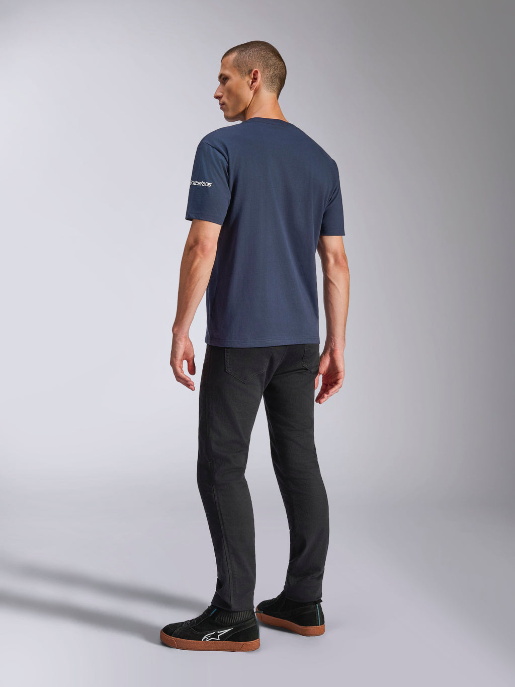 Alpinestars Frontal CSF Tee, t-shirt met korte mouwen, marineblauw, achteraanzicht op model met logo op de mouw, gedragen met zwarte broek en sneakers, casual streetwear geïnspireerd op de motorsport