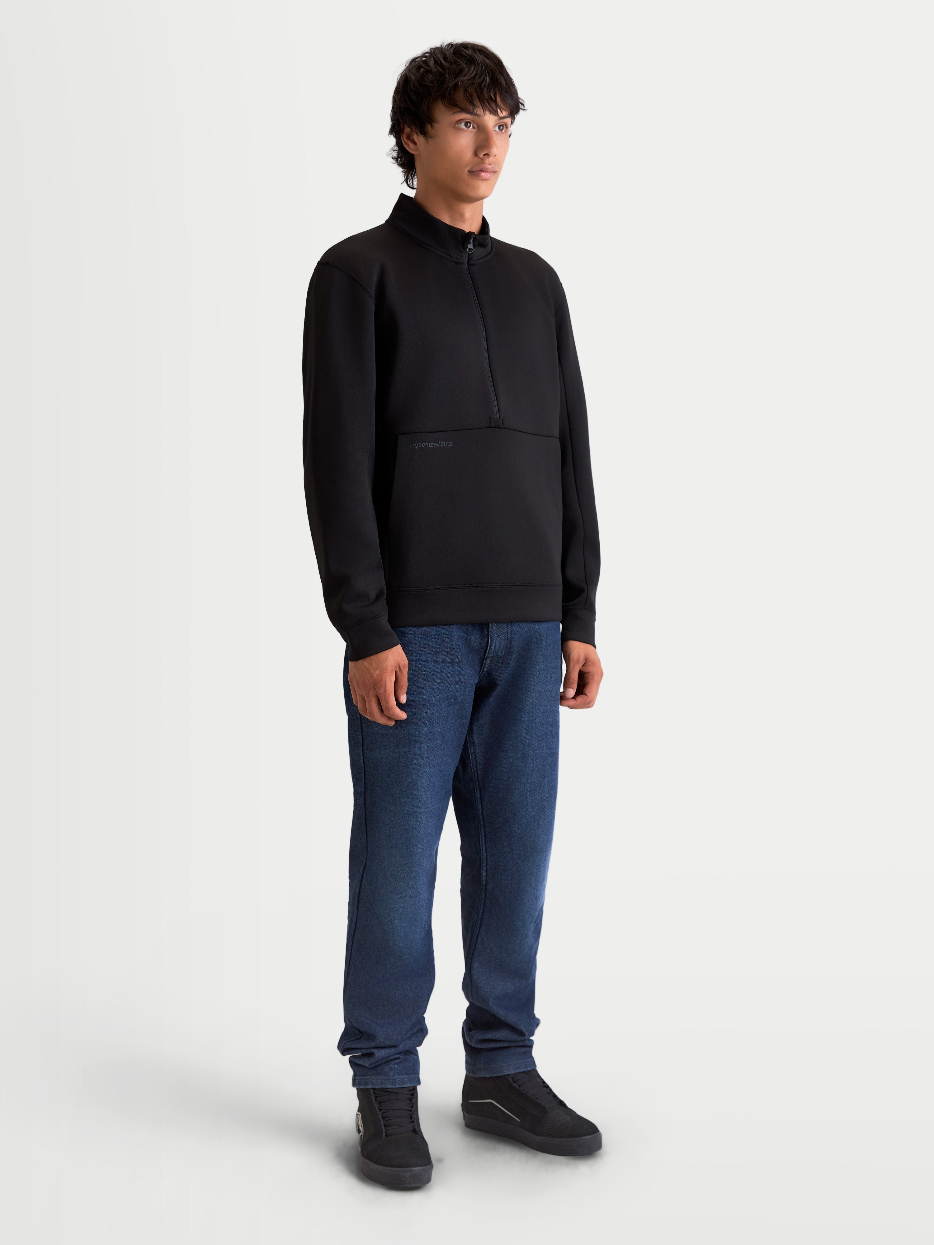 Alpinestars Sweat Half-Zip Apera, pull sportswear premium noir, style inspiré du sport automobile, unisexe, construction en polaire tri-mélange avec fermeture demi-zippée et poche kangourou, porté par un modèle