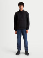 Alpinestars Sweat Half-Zip Apera, pull sportswear pour homme, noir, avec fermeture demi-zippée et poche kangourou, style inspiré du sport automobile pour un confort décontracté, porté par un modèle avec un jean bleu.