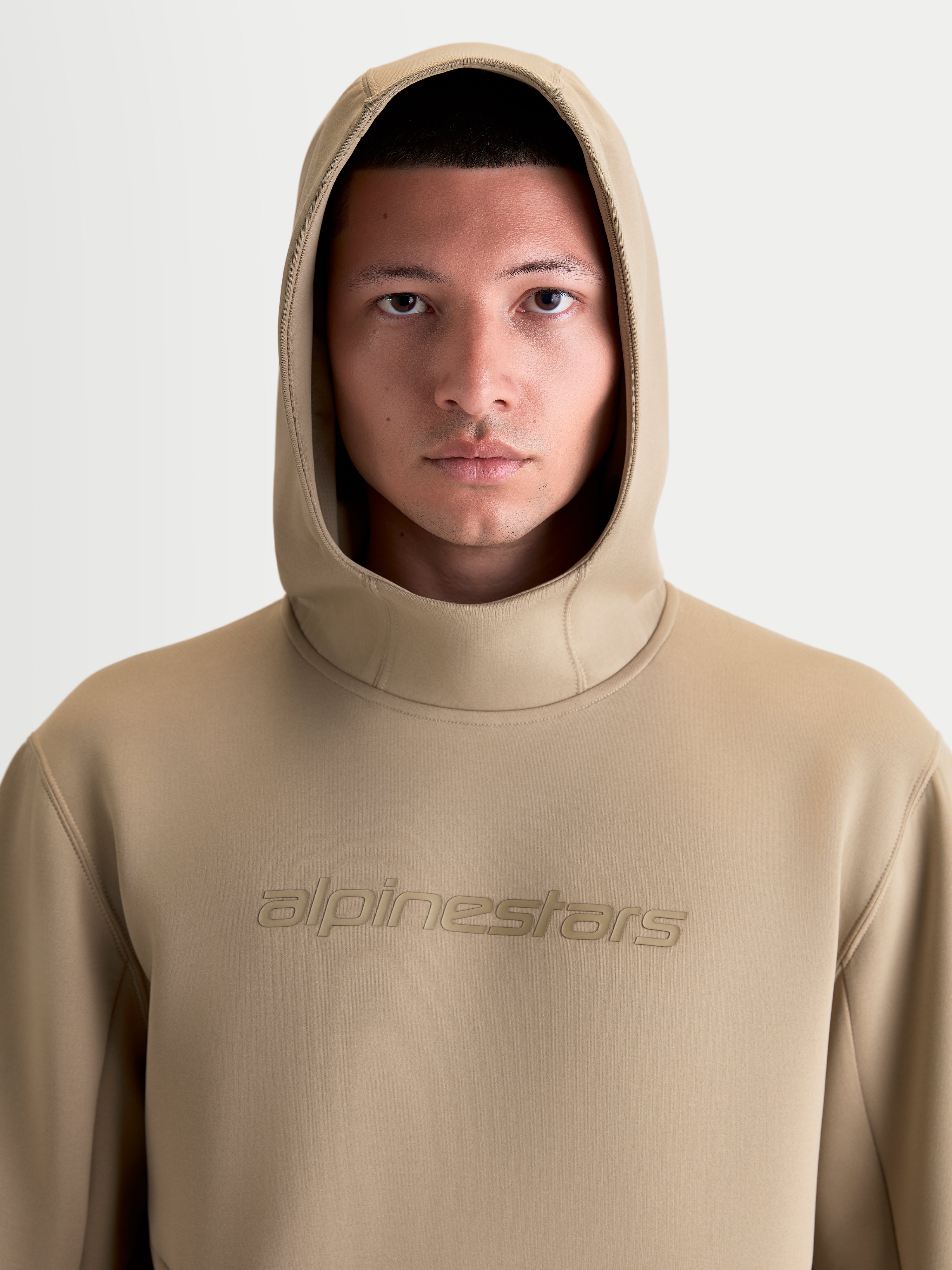 Alpinestars Sweat à capuche Datrix, pull sportswear décontracté pour homme et femme, marron, gros plan de face sur un modèle avec la capuche relevée, marquage Alpinestars ton sur ton et matière polaire premium tri-mélange.