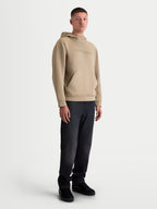 Alpinestars sweat à capuche Datrix, sweat à capuche de sportswear pour homme, marron clair, logo HD ton sur ton, capuche doublée en mesh et poche avant avec détail de pli, porté par un modèle pour un style décontracté inspiré du sport automobile.
