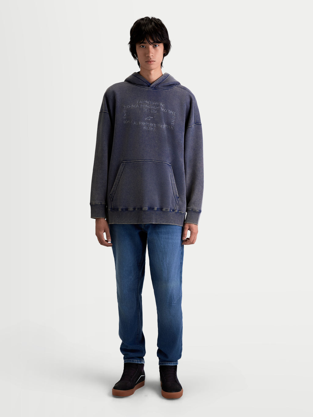 Alpinestars Sweat À Capuche Infinite Washed Oversize, vêtement sportswear pour homme porté par un mannequin, bleu marine délavé avec finition effet neige, doté d'une poche kangourou et du logo Alpinestars brodé sur la poitrine, coupe oversize décontractée en polaire premium.