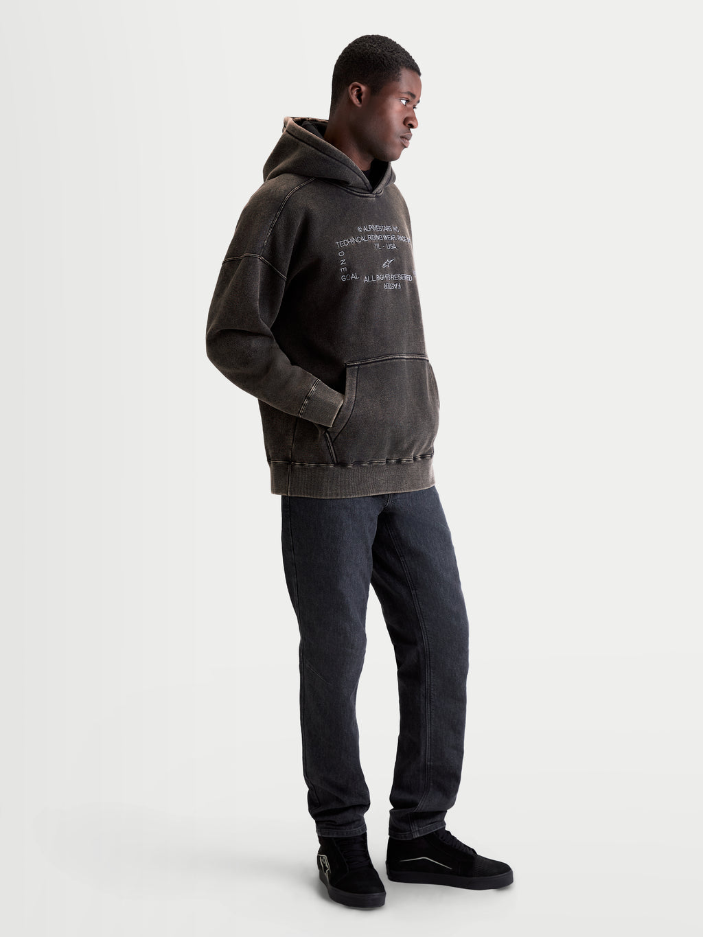 Alpinestars sweat à capuche Infinite Washed Oversize, sweat sportswear pour homme, noir délavé avec finition effet neige, logo brodé blanc sur la poitrine, poche kangourou, modèle de profil.