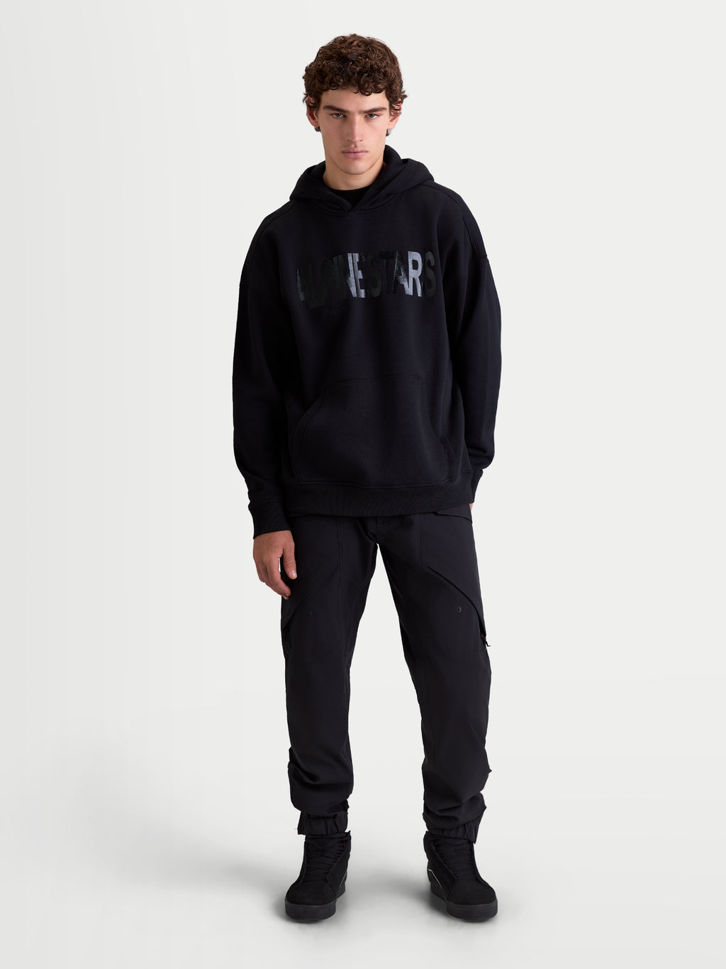 Alpinestars sweat à capuche Shaw Oversized, pull de sportswear pour homme, noir, coupe ample en polaire avec logo Alpinestars texturé sur la poitrine, poche kangourou et capuche doublée, vue de face sur modèle