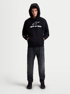Alpinestars Prelude Oversized, sweat à capuche de sportswear en polaire unisexe, noir et blanc, coupe ample avec poche kangourou et logos en impression en relief sur la poitrine et la manche, porté par un modèle