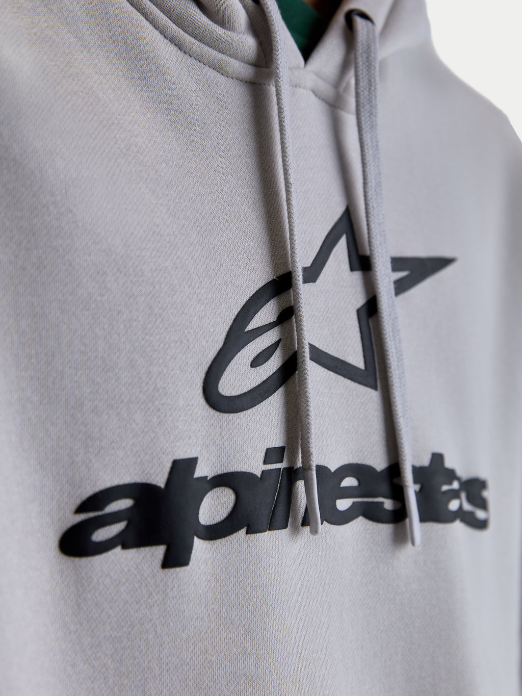 Alpinestars Prelude oversized hoodie, close-up detail van het zwarte puff-print logo en de ster-graphic op cementgrijs fleece, voorzien van platte trekkoorden, premium unisex lifestyle sportswear hoodie.