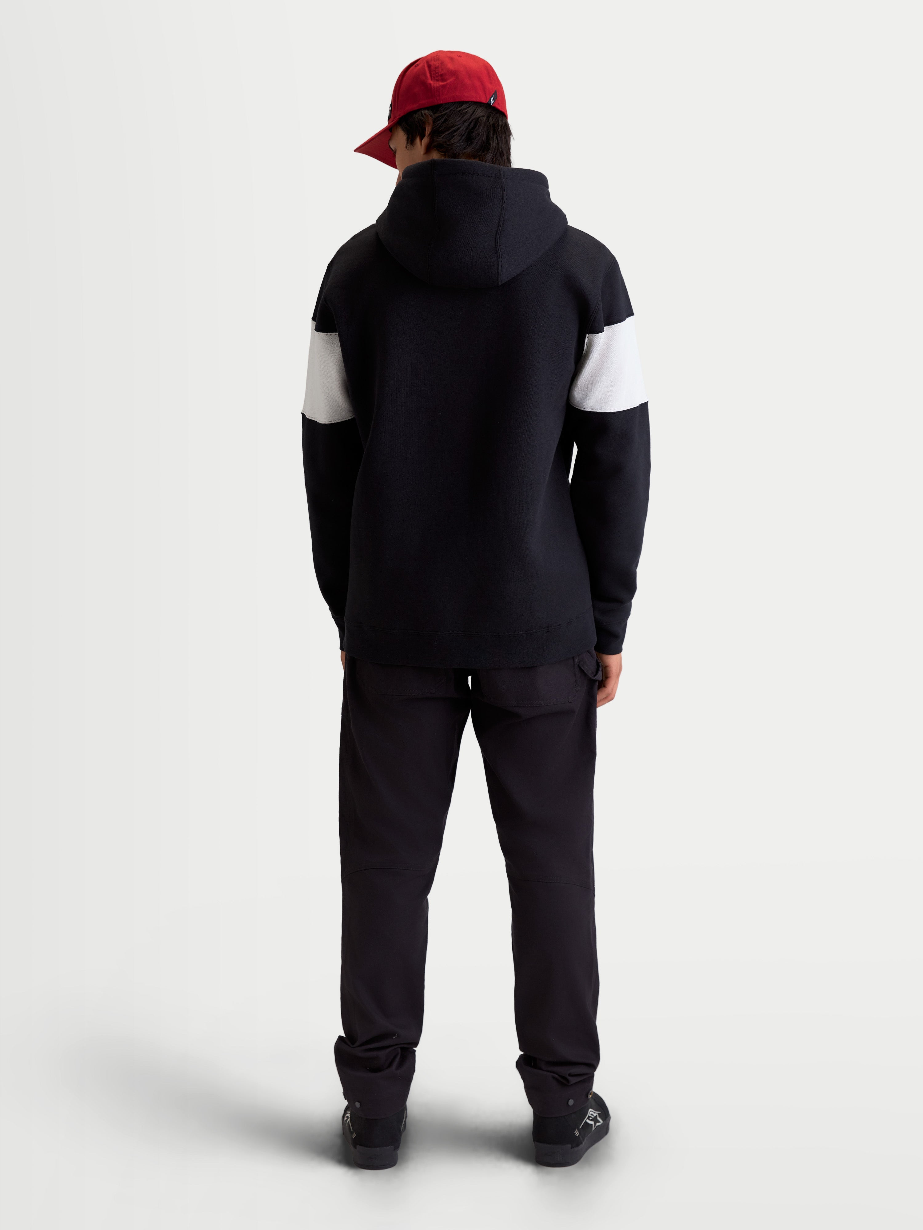 Alpinestars Sweat à capuche Cubic, sweat à capuche sportswear mixte, noir et blanc, vue de dos sur modèle portant une casquette rouge, manches avec blocs de couleurs contrastés, construction en polaire de coton mélangé.
