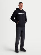 Alpinestars Sweat à capuche Race Wordmark, sweat à capuche polaire de sportswear pour homme, noir et blanc, logo linéaire blanc sur la poitrine, capuche avec cordons de serrage et poche kangourou frontale, porté par un modèle.