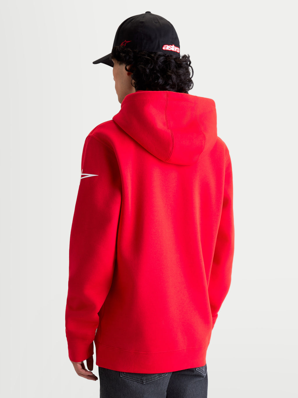 Alpinestars Race Wordmark Hoodie, sportswear hoodie van fleece, rood en wit, achteraanzicht op model met de capuchon en het witte Ageless-logo op de mouw, premium katoen en gerecycled polyester voor een casual motorsportstijl.