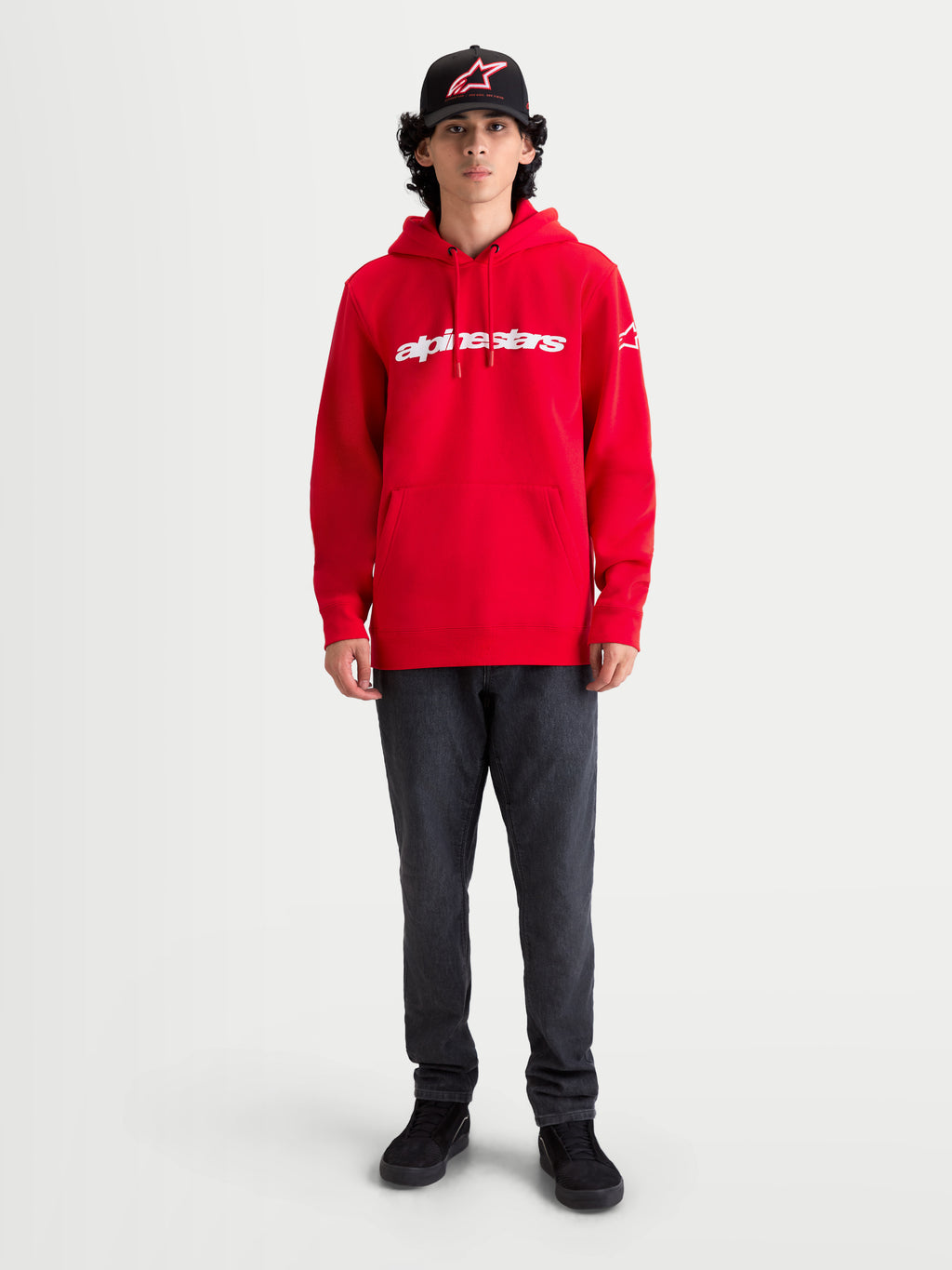 Alpinestars Race Wordmark hoodie, sportswear pullover fleece in rood met wit Alpinestars woordmerklogo, voorzien van een kangoeroezak en verstelbare capuchon met trekkoord, gedragen door een model voor een casual motorsport-geïnspireerde look.