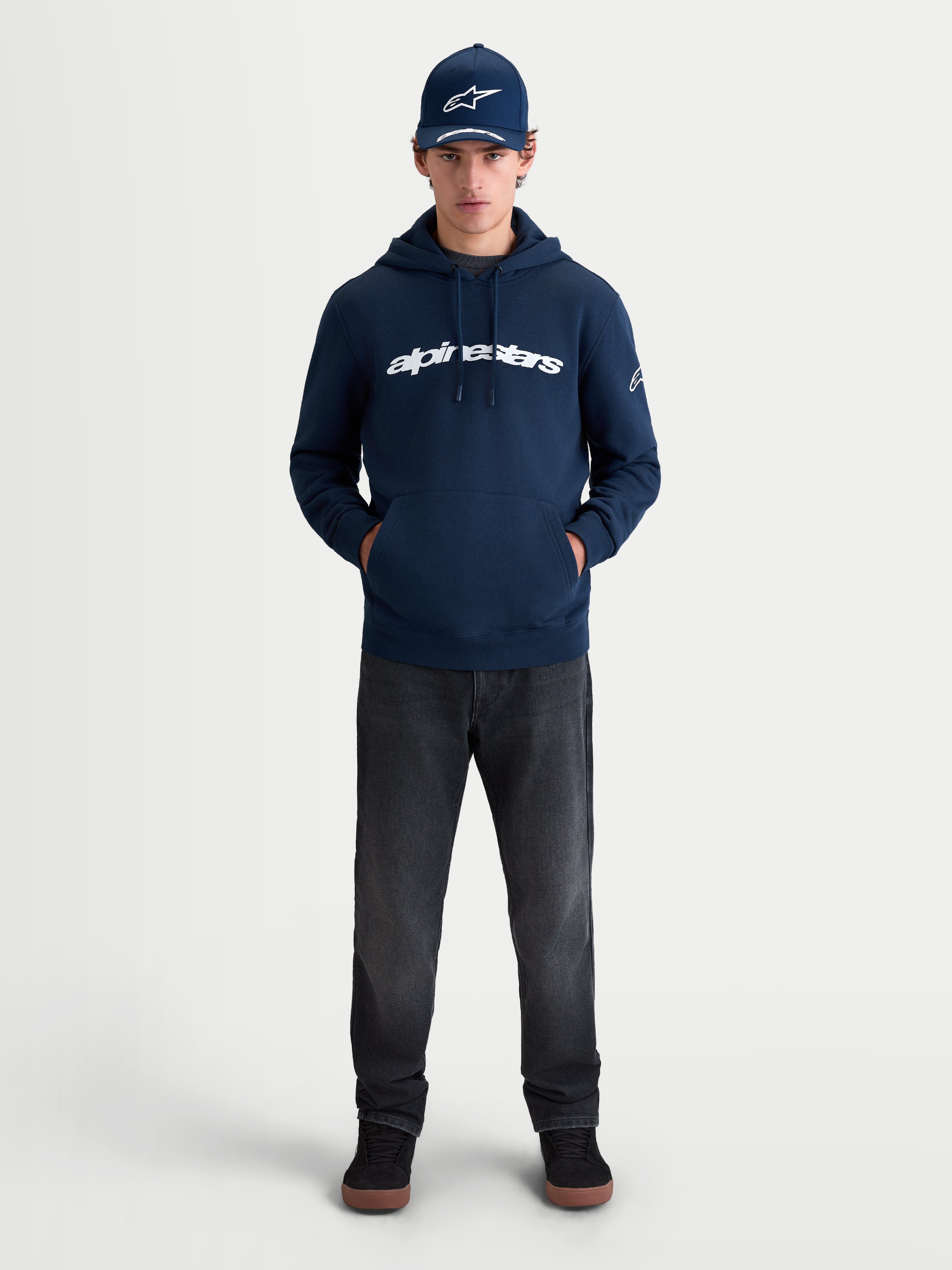 Alpinestars Race Wordmark Hoodie, Sportswear Pullover Fleece for Men and Women, Navy Blue and White, featuring a bold front wordmark graphic and Ageless sleeve logo, on-model lifestyle view for a casual motorsport-inspired look.