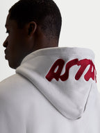 Alpinestars Sweat à capuche Pioneer Oversized, polaire de sportswear décontractée pour homme et femme, gris ciment avec logo brodé rouge sur la capuche, vue de dos sur modèle mettant en avant la coupe oversized et le marquage premium
