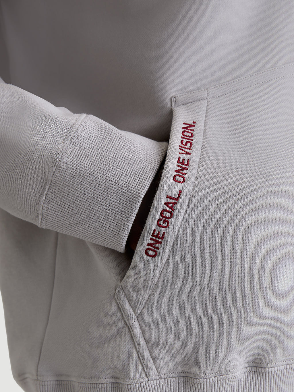 Alpinestars Sweat à capuche Pioneer Oversized, polaire sportswear grise et rouge, détail de la poche kangourou avec texte brodé 'ONE GOAL. ONE VISION.' et poignet côtelé, vêtement lifestyle premium pour passionnés de sports mécaniques