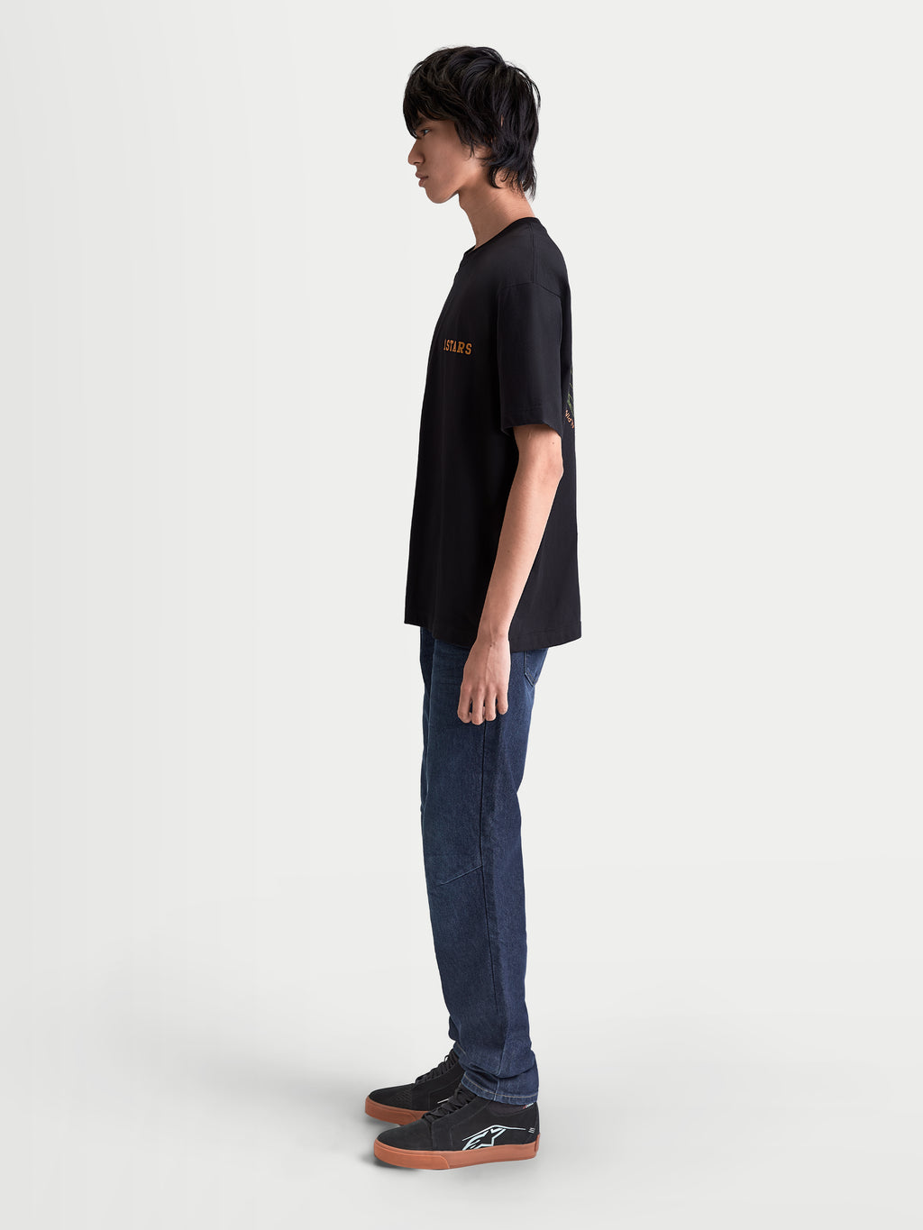 Alpinestars Latitude Oversized CSF t-shirt, heren-t-shirt met korte mouwen, zwart met oranje Astars-graphic, zijprofiel op model, relaxte oversized pasvorm, casual alledaagse stijl