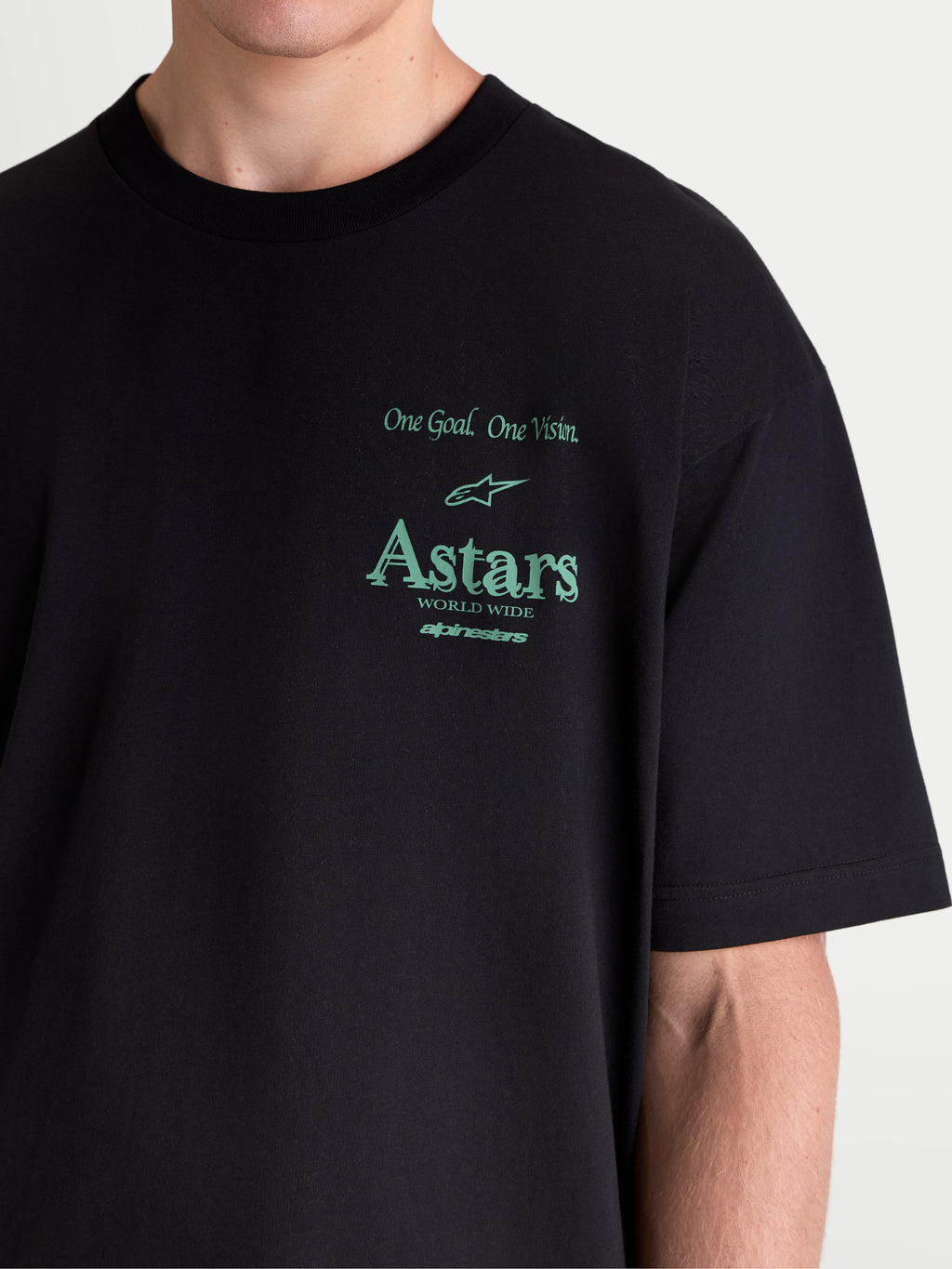 Alpinestars T-Shirt Post Oversized CSF, t-shirt sportswear à manches courtes, noir et vert, gros plan sur modèle montrant la coupe oversize, inscriptions One Goal. One Vision. et logos Astars, construction en mélange de coton doux.