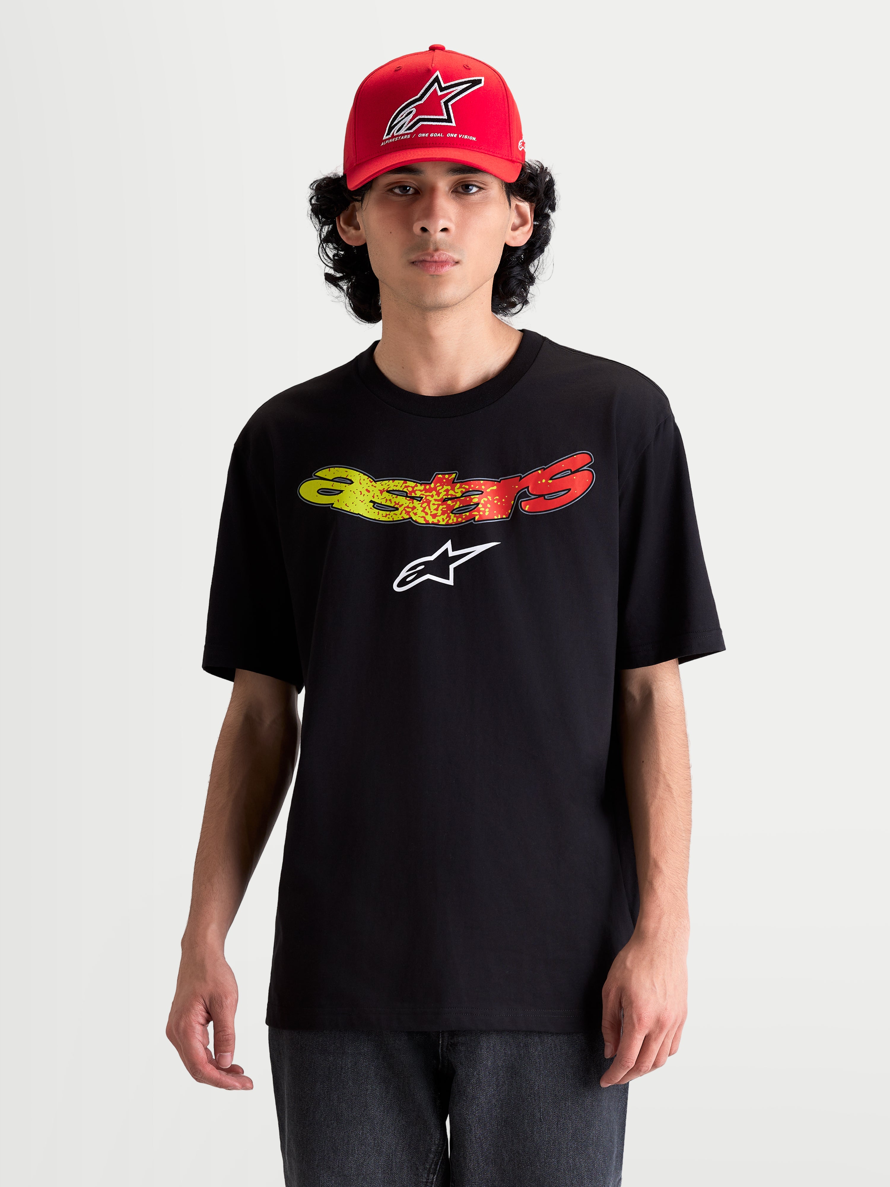Alpinestars T-Shirt Elliptogrit CSF, t-shirt à manches courtes sportswear pour homme, noir avec lettrage Astars incurvé en dégradé de rouge et jaune, logo Astars blanc, mélange coton-polyester, style décontracté porté sur modèle.