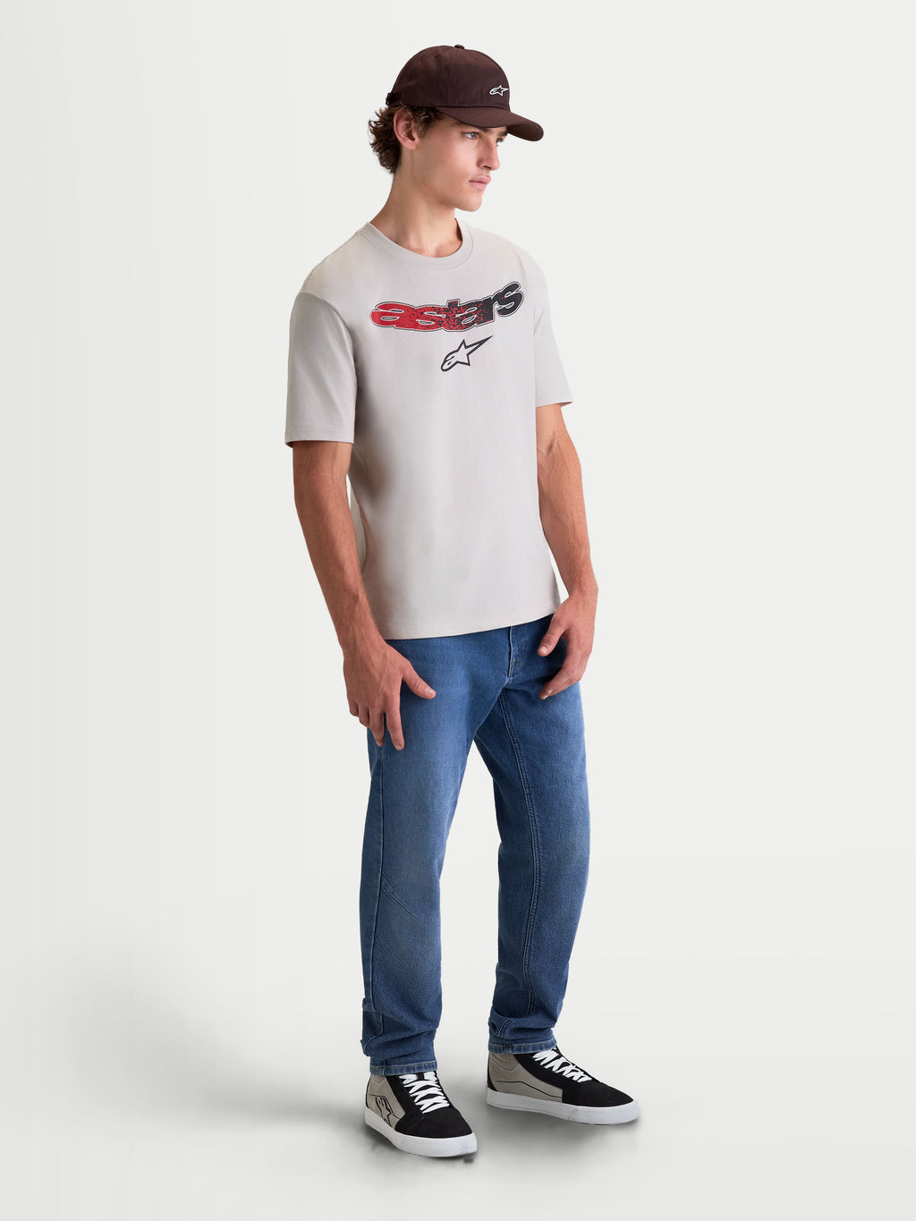 Alpinestars T-Shirt Elliptogrit CSF, t-shirt sportswear à manches courtes, gris ciment, avec logo Astars incurvé et dégradé rouge et noir, photo plein pied sur modèle pour un look lifestyle décontracté inspiré du sport automobile.