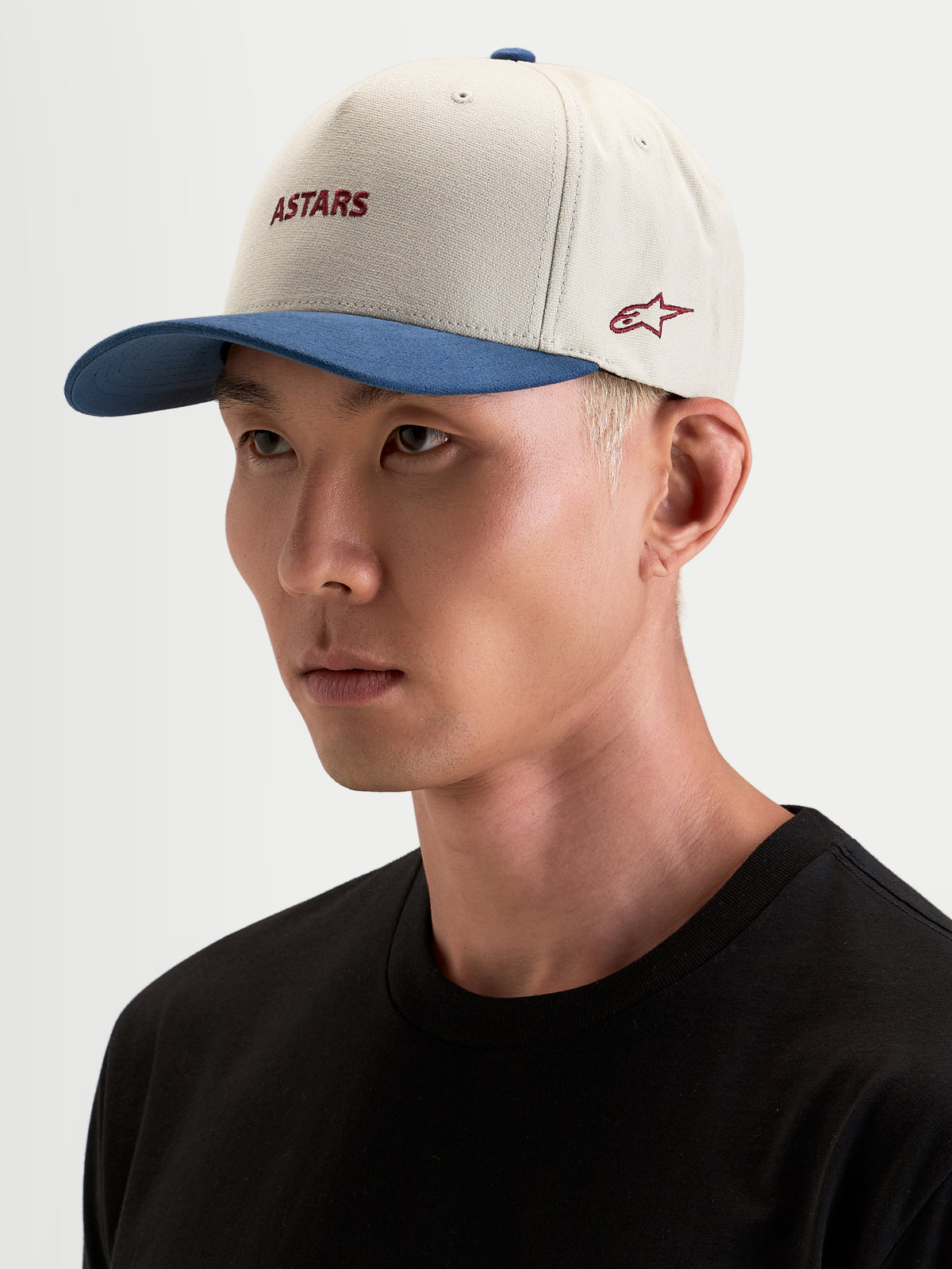 Alpinestars County Canvas pet, sportswear pet in zand en blauw, gedragen door een model, met een gebogen klep en geborduurde Astars-logo's