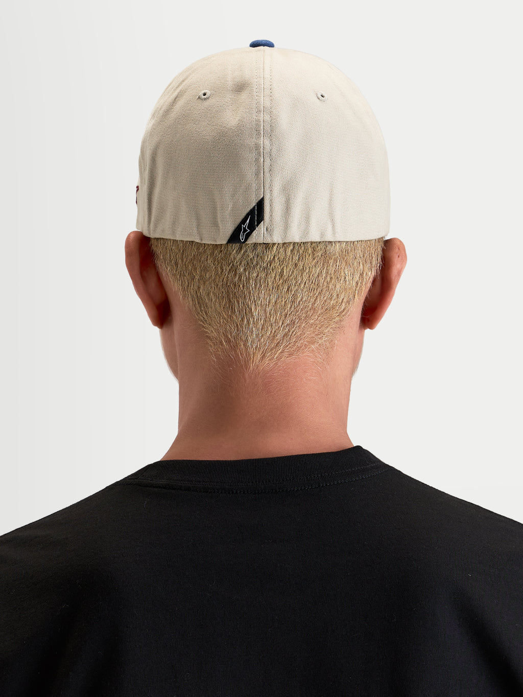 Alpinestars County Canvas Pet, casual sportswear pet, achteraanzicht gedragen door een model met flex-back-pasvorm en subtiel label op de achterkant, zandkleurig en blauw, oxford peached katoenen stof