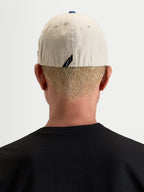 Alpinestars County Canvas Pet, casual sportswear pet, achteraanzicht gedragen door een model met flex-back-pasvorm en subtiel label op de achterkant, zandkleurig en blauw, oxford peached katoenen stof