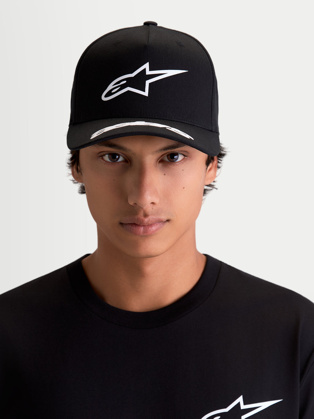 Alpinestars Arclight, casquette de sportswear noire et blanche, vue de face sur modèle. Comprend un logo Astars blanc en relief sur une couronne structurée, une visière incurvée avec détails et un tissu en sergé premium.