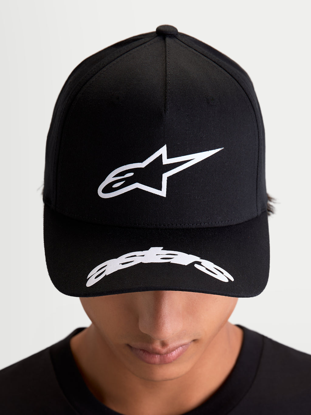 Alpinestars Arclight, casquette de sportswear noire et blanche, portée par un modèle, vue de face montrant le logo Astars blanc en relief texturé sur une couronne structurée et logo incurvé sur la visière, style décontracté inspiré du motorsport