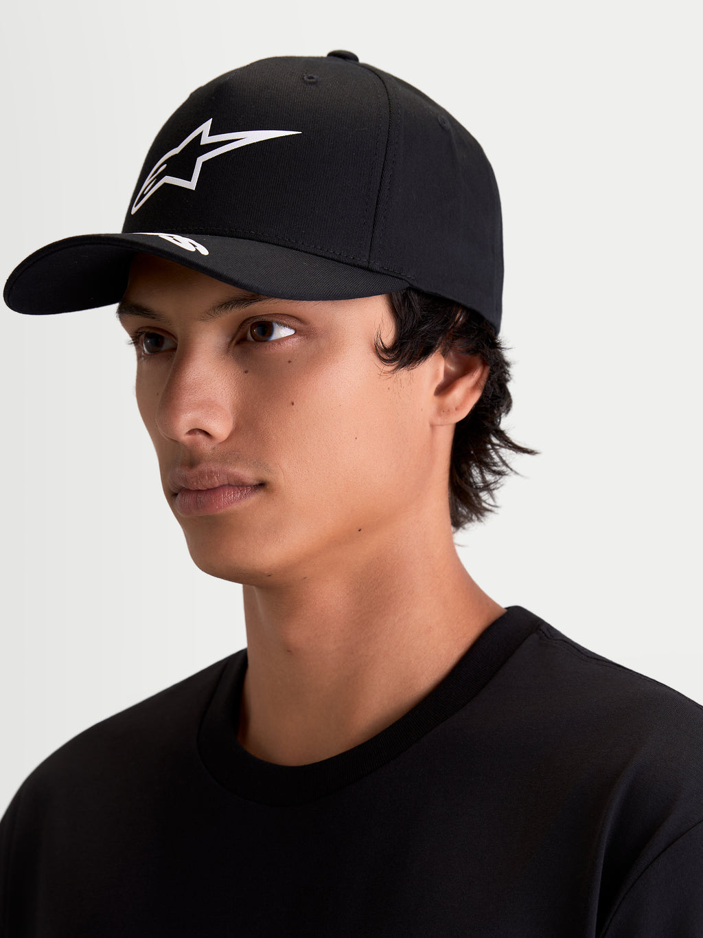 Alpinestars Arclight, casquette de sportswear pour homme et femme, noire et blanche, avec visière incurvée et couronne structurée, logo Astars blanc texturé en relief, portée par un modèle