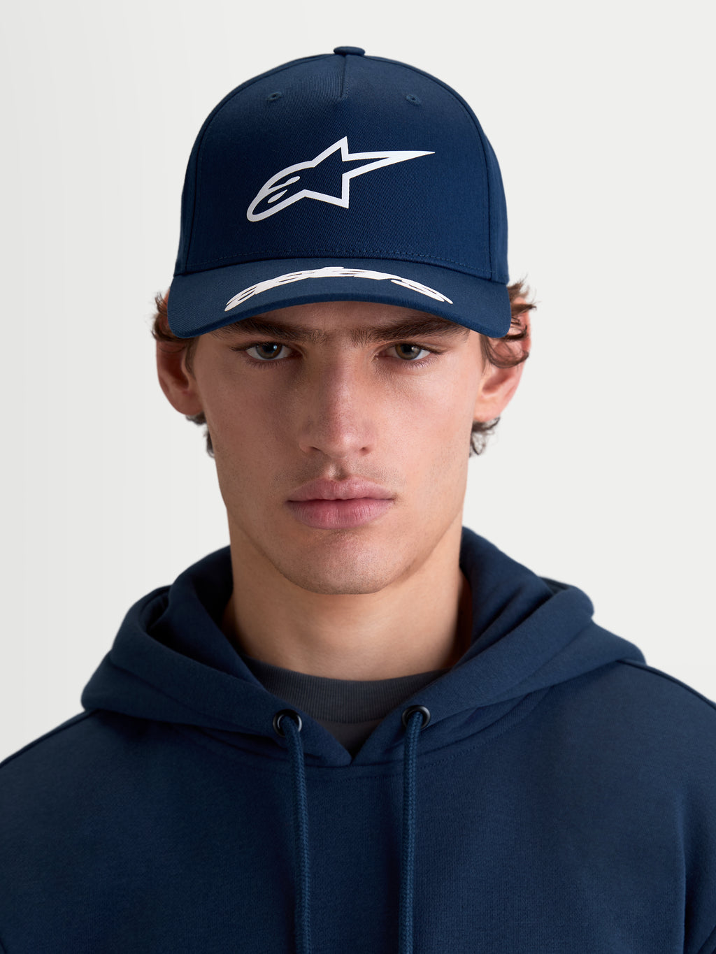 Alpinestars Arclight, casquette de sportswear à visière incurvée, bleu marine et blanche, vue de face portée par un modèle, avec couronne structurée, logo Astars en relief texturé et sergé de coton premium