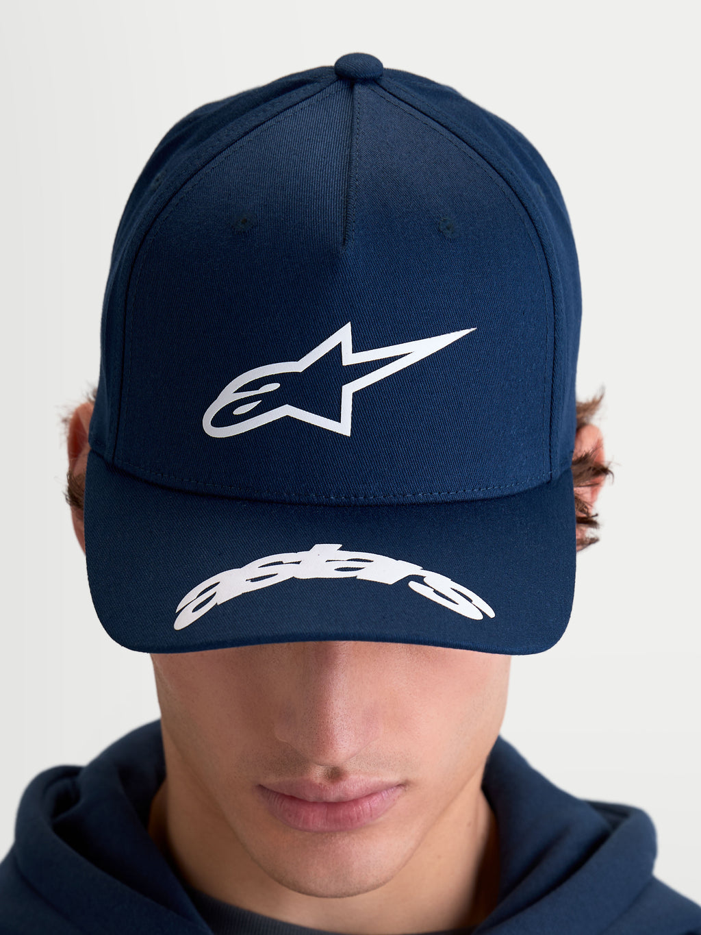 Alpinestars Arclight, casquette sportswear de style motorsport, bleu marine et blanche, avec logo Astars blanc en relief sur la couronne structurée et lettrage sur la visière incurvée, vue de face sur modèle