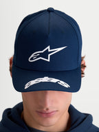 Alpinestars Arclight, casquette sportswear de style motorsport, bleu marine et blanche, avec logo Astars blanc en relief sur la couronne structurée et lettrage sur la visière incurvée, vue de face sur modèle