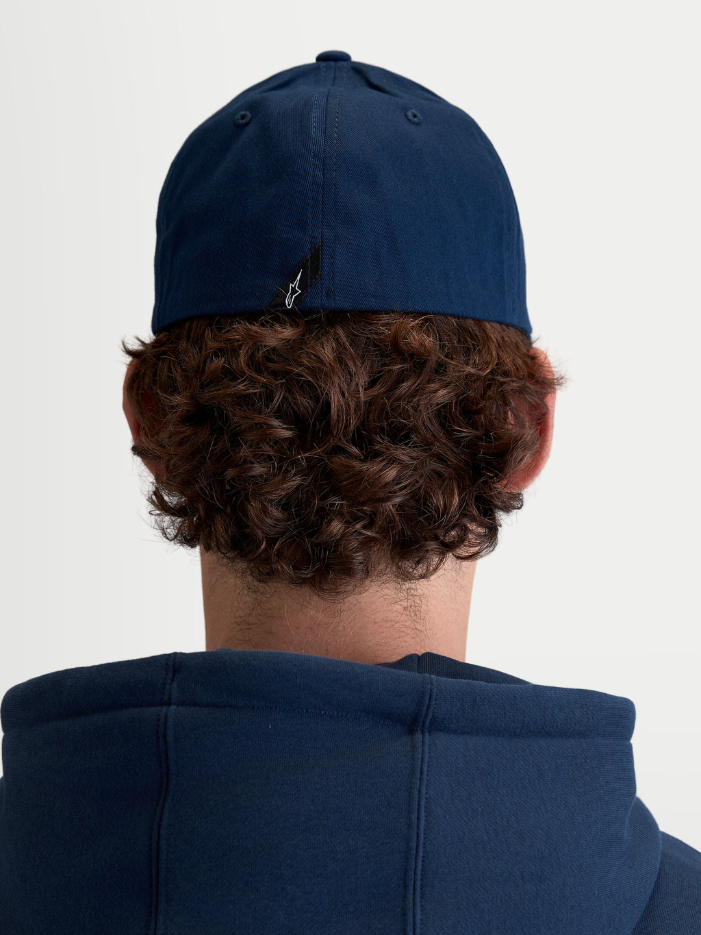 Alpinestars Arclight, casquette de sportswear unisexe, bleu marine, confectionnée en sergé de coton durable avec dos flexible, vue de dos sur modèle montrant le détail de l'étiquette avec le logo Astars.