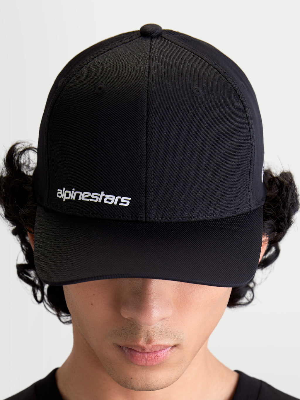 Alpinestars Points, casquette sportswear noire portée par un modèle, logo Alpinestars blanc sur le devant, visière incurvée et construction en nylon tactel léger.