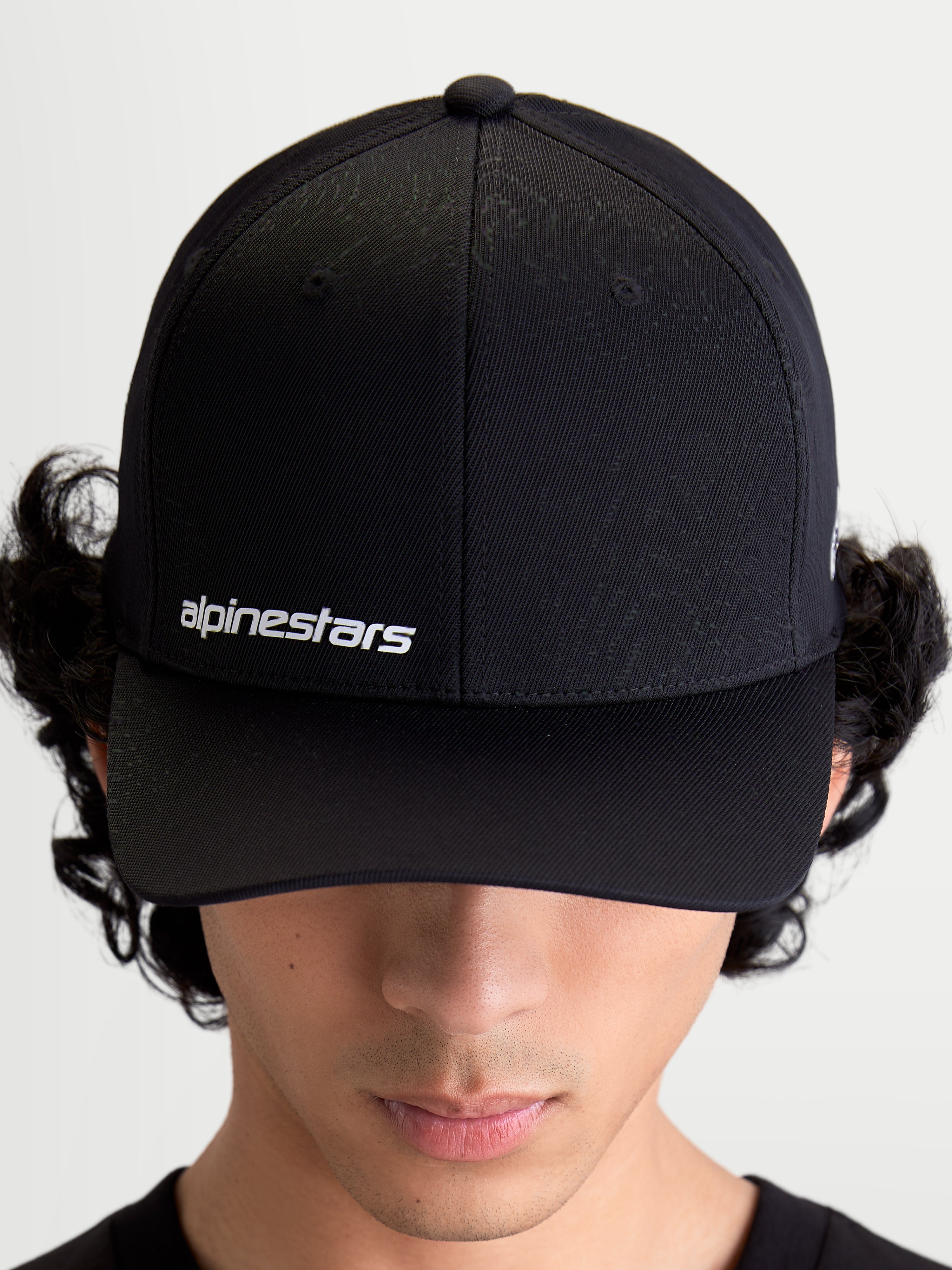 Alpinestars Points, casquette sportswear noire portée par un modèle, logo Alpinestars blanc sur le devant, visière incurvée et construction en nylon tactel léger.