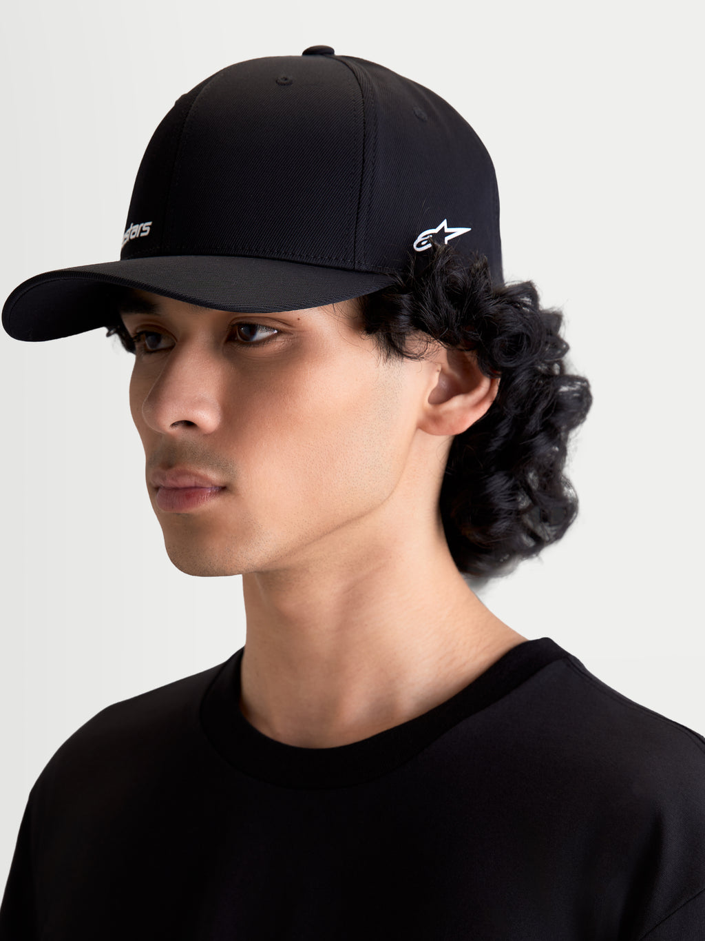 Alpinestars casquette Points, casquette sportswear unisexe noire avec logos blancs, vue de profil sur mannequin, visière incurvée, nylon tactel léger et coupe flex-back, style motorsport décontracté
