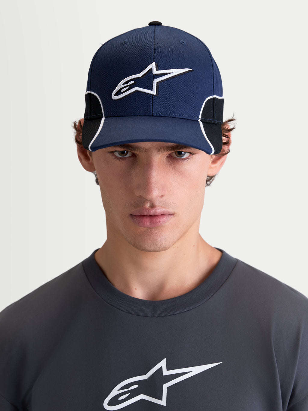 Alpinestars 500 Snapback pet, herensportswear baseballpet, donkerblauw en zwart, gebogen klep, gestructureerde kroon, 3D-geborduurd Astars-logo en witte contrasterende biezen, vooraanzicht op model.