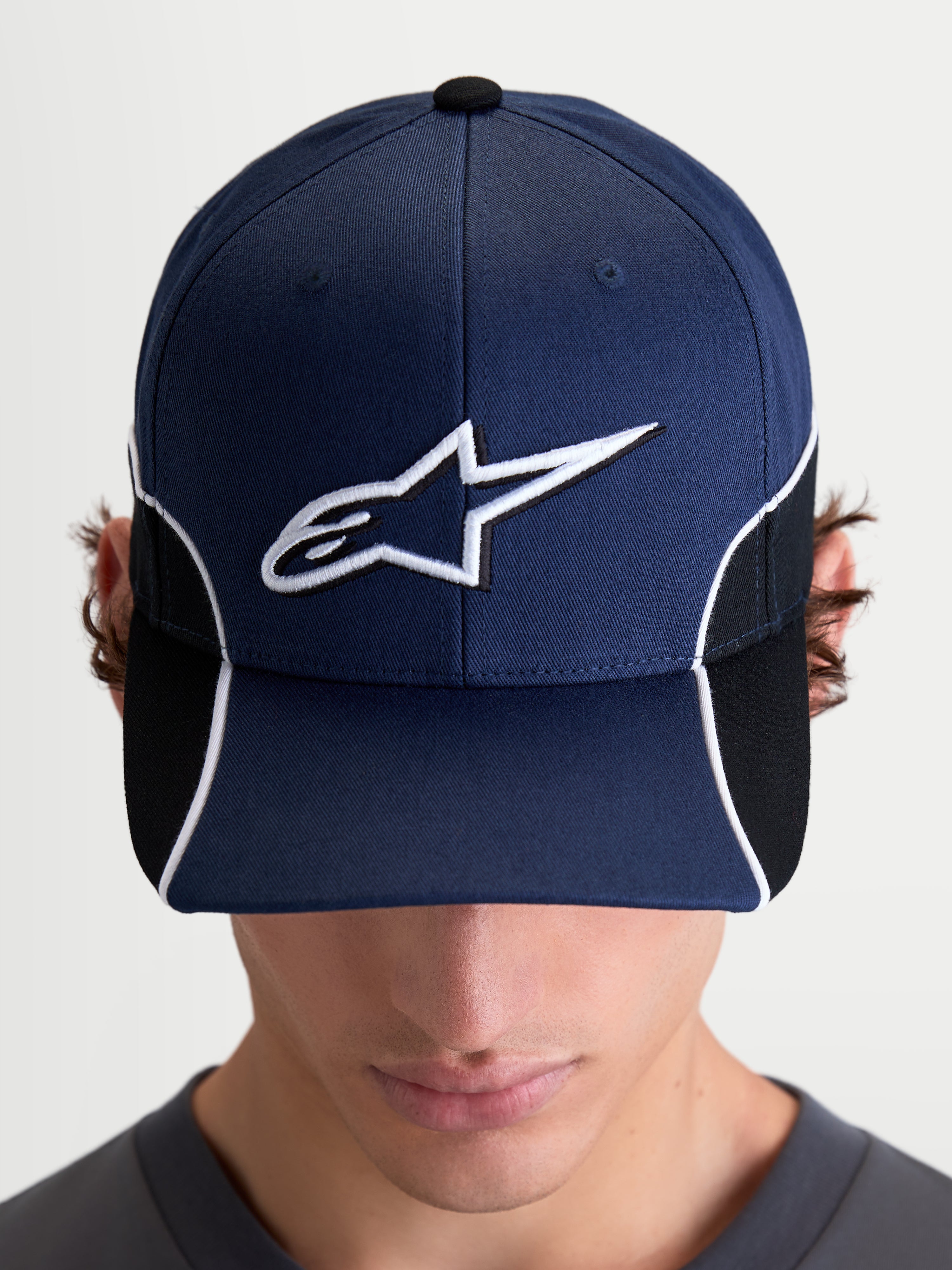 Alpinestars 500 Snapback pet, motorsport-geïnspireerde sportswear pet, unisex, marineblauw en zwart, met een gebogen klep en 3D-geborduurd wit Astars-logo, contrasterende biezen en cut-and-sew details, vooraanzicht op model.